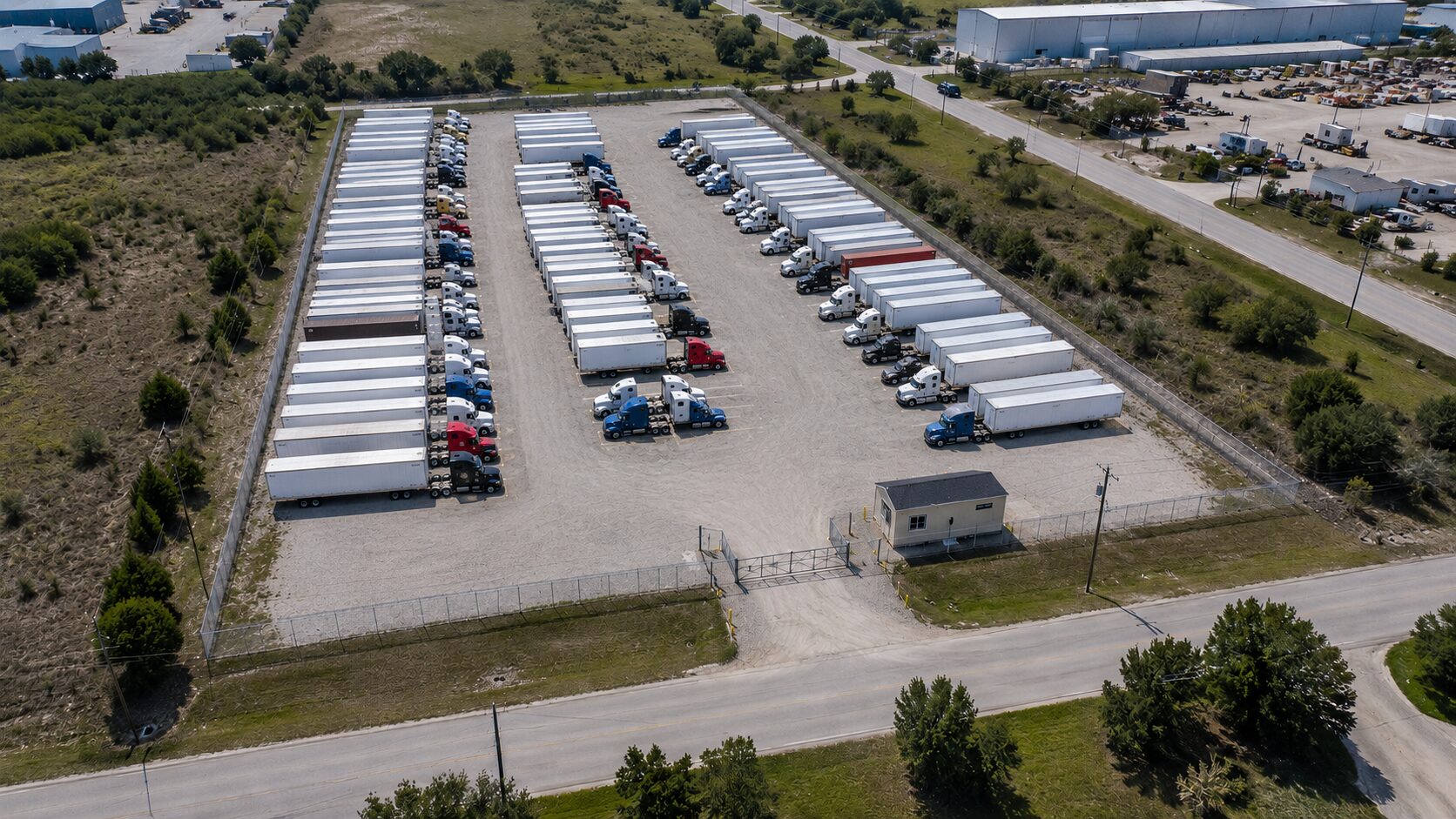 Illustrative aerial rendering of a representative secured truck-and-trailer yard: rows of parked trailers and tractors on a graveled lot behind a fenced, gated entrance. Not a photograph of the actual St George site.